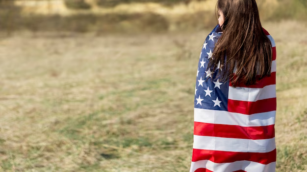 A woman wrapped in a usa flag stands on a field